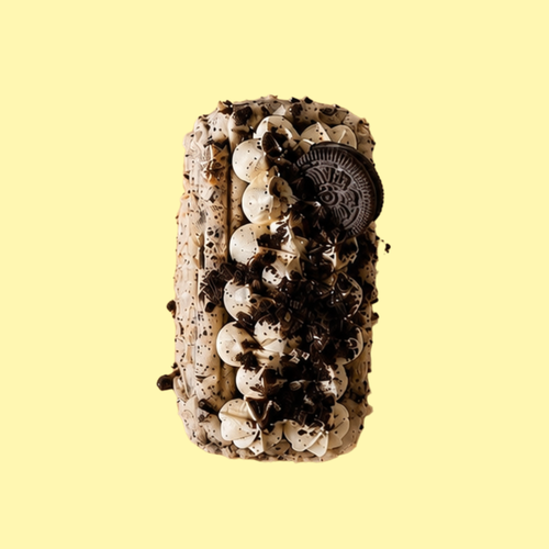 An Oreo-themed basque cheesecake with white frosting, dark chocolate cookie crumbs, and a whole Oreo cookie on top, presented on a solid pale yellow background.