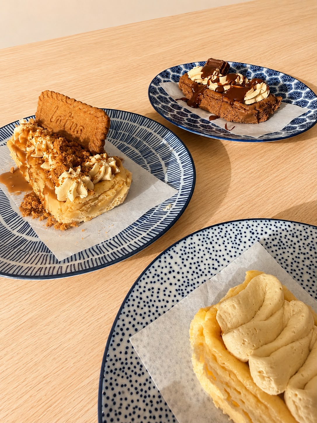 Three blue and white decorated plates with slices of basque cheesecakes with toppings. 